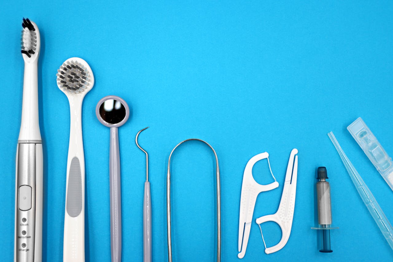 Flat lay of dental care tools including toothbrushes, dental mirror, and floss sticks on blue background.