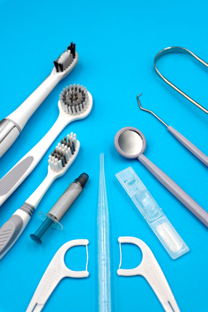 A flat lay of various dental care tools including toothbrush, floss, and dental pick on blue background.