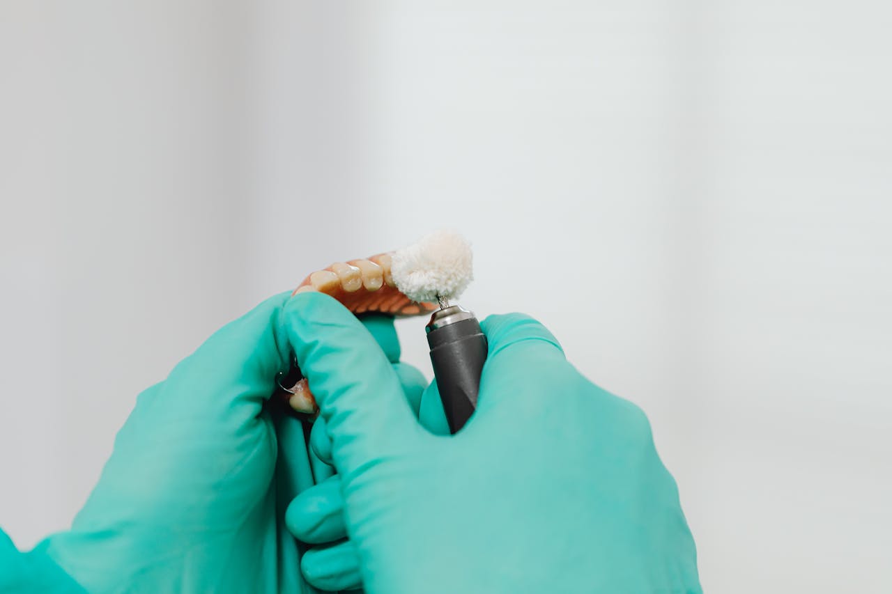 A close-up view of hands with latex gloves polishing a denture using a dental instrument.